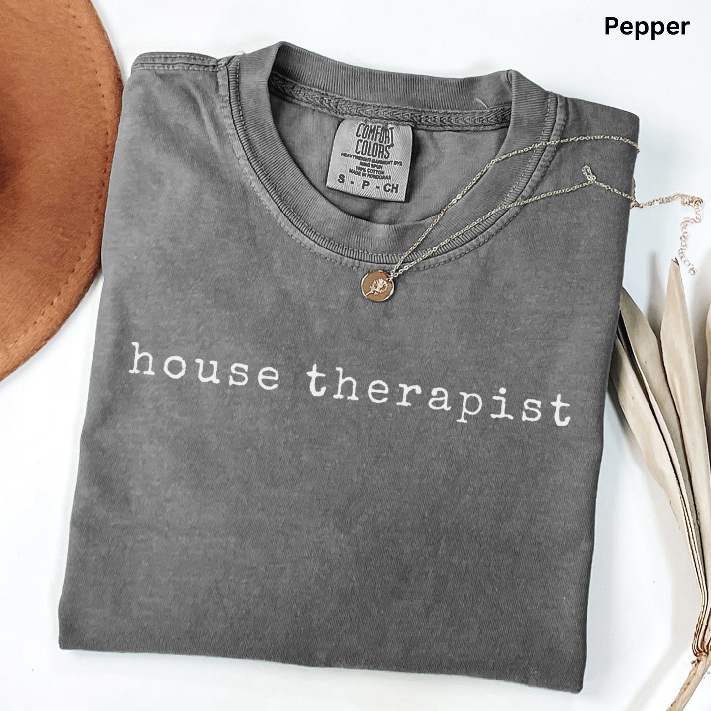 A gray t-shirt with the text "house therapist" printed on it, along with a small pendant necklace.