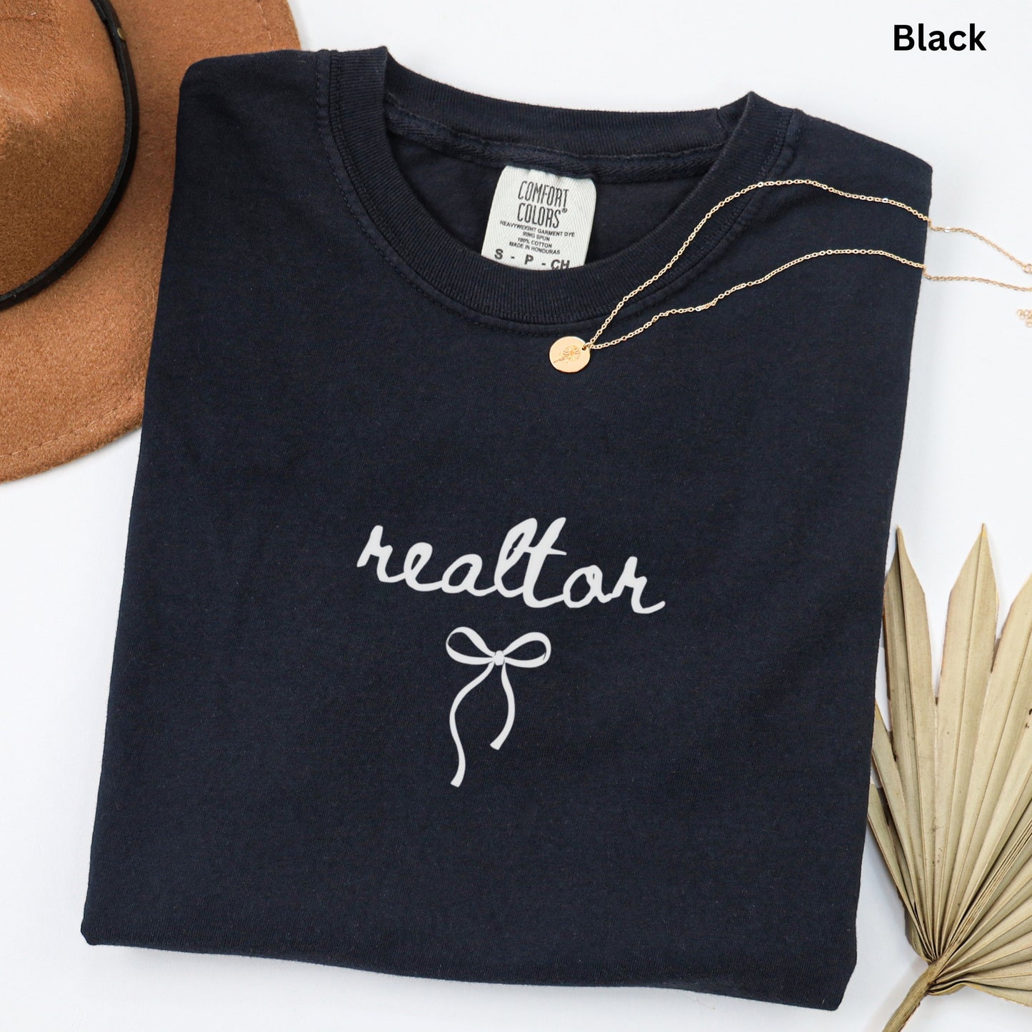 a black t-shirt with the word "realtor" printed on it, along with a gold necklace and a brown hat.