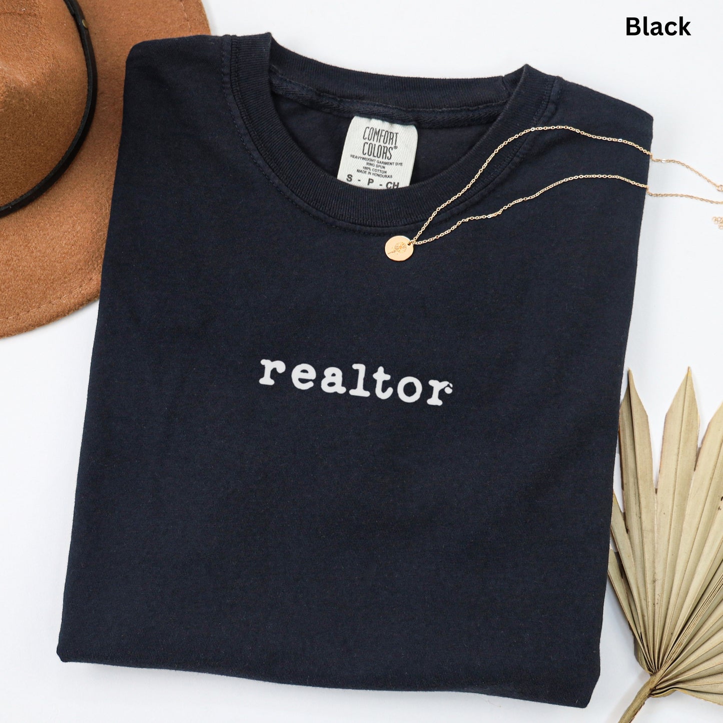 a black t-shirt with the word "realtor" printed on it, along with a brown hat and a leaf.
