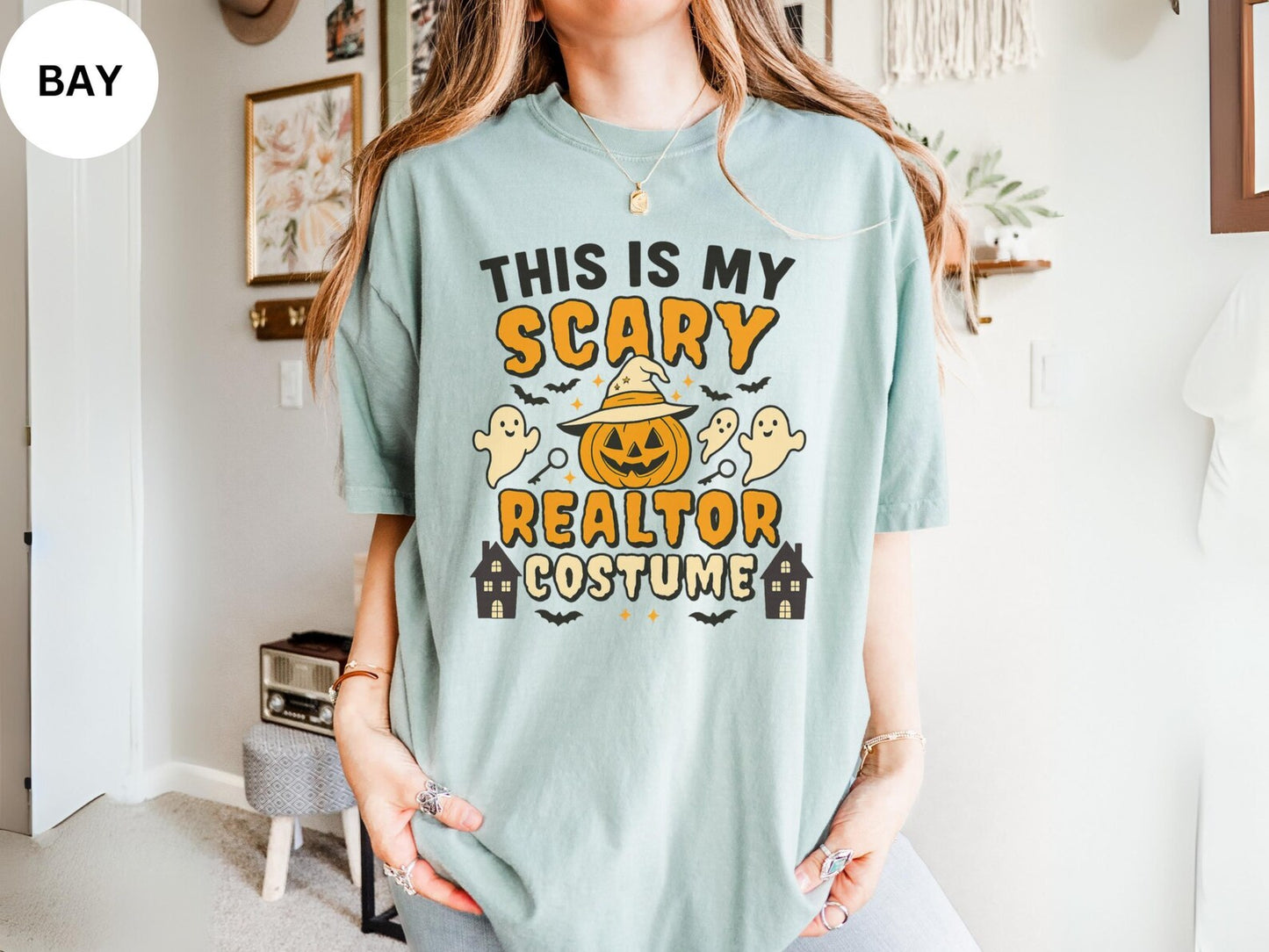 A person wearing a light blue t-shirt with a Halloween-themed design, including a jack-o-lantern, ghost, and houses.