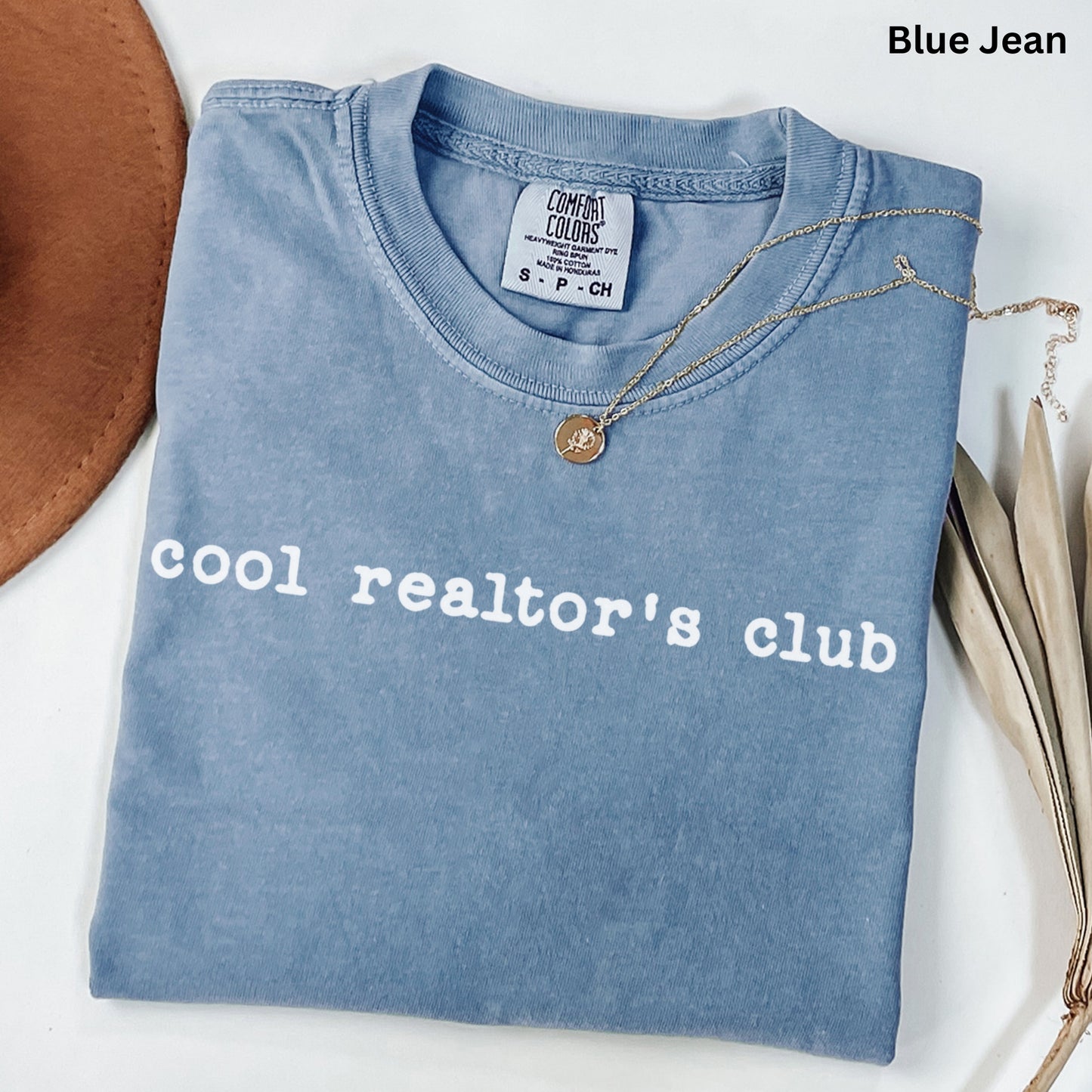 A blue t-shirt with the text "cool realtor's club" printed on it, along with a small gold medallion necklace.