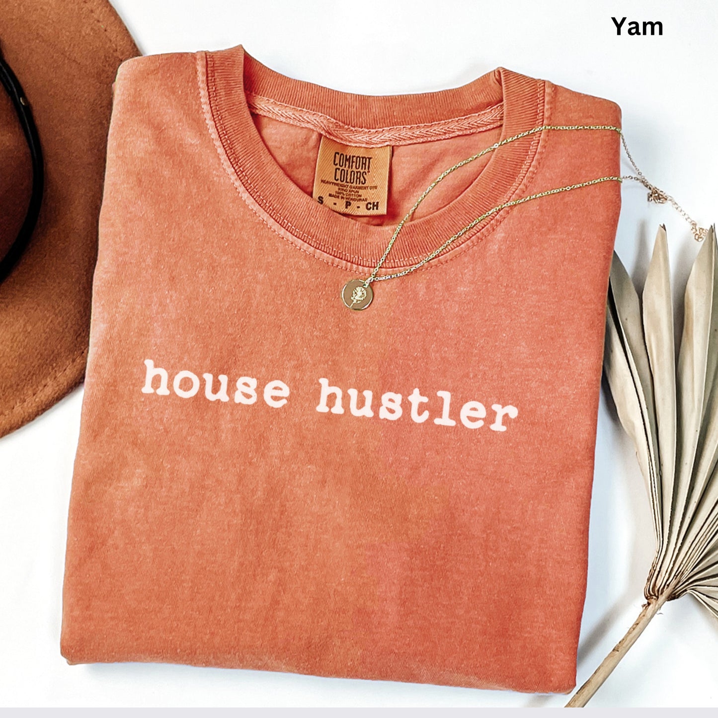 a red t-shirt with the text "house hustler" printed on it, along with a necklace and a hat.