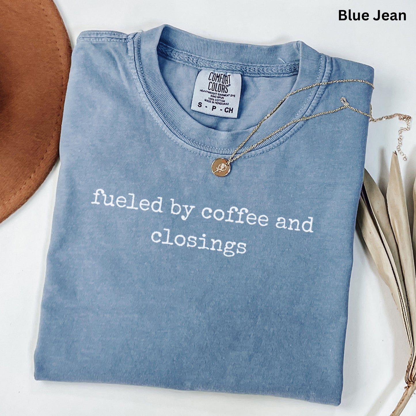 A blue t-shirt with the text "fuelled by coffee and closings" printed on it, along with a necklace and some leaves.