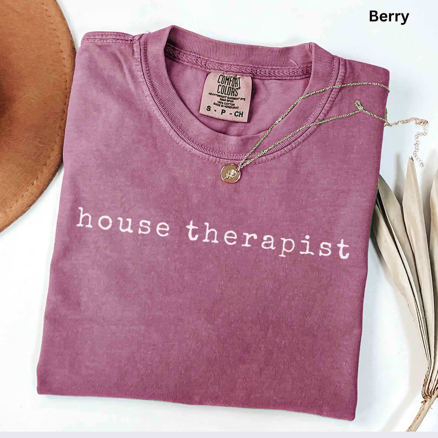 A pink t-shirt with the text "house therapist" printed on it, along with a necklace and a hat.