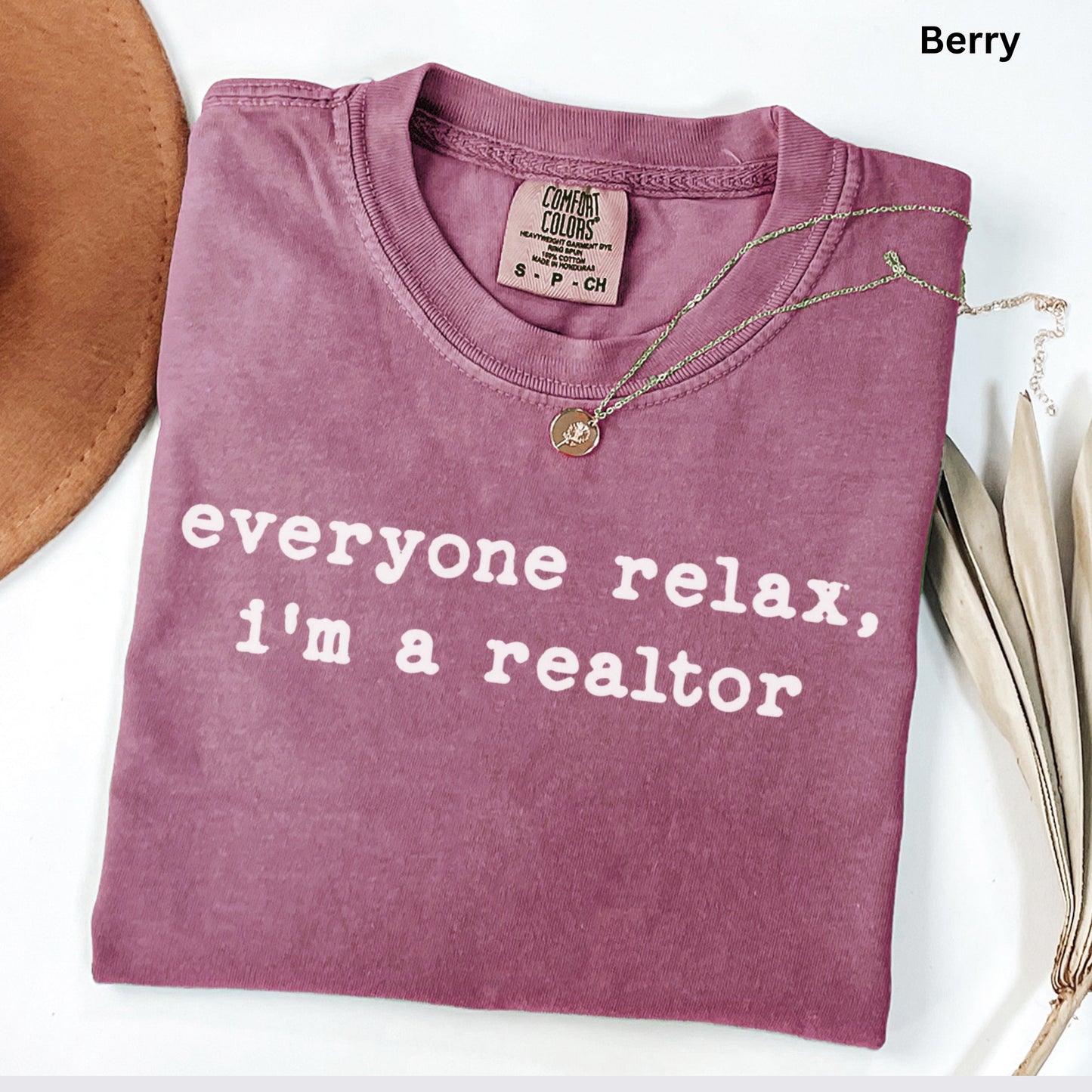A purple t-shirt with the text "Everyone relax, I'm a realtor" printed on it, along with a necklace and a hat.