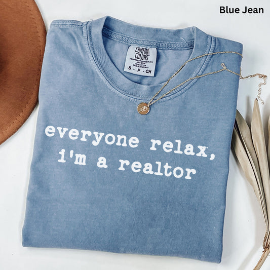 A blue t-shirt with the text "Everyone relax, I'm a realtor" printed on it, along with a necklace and some leaves.