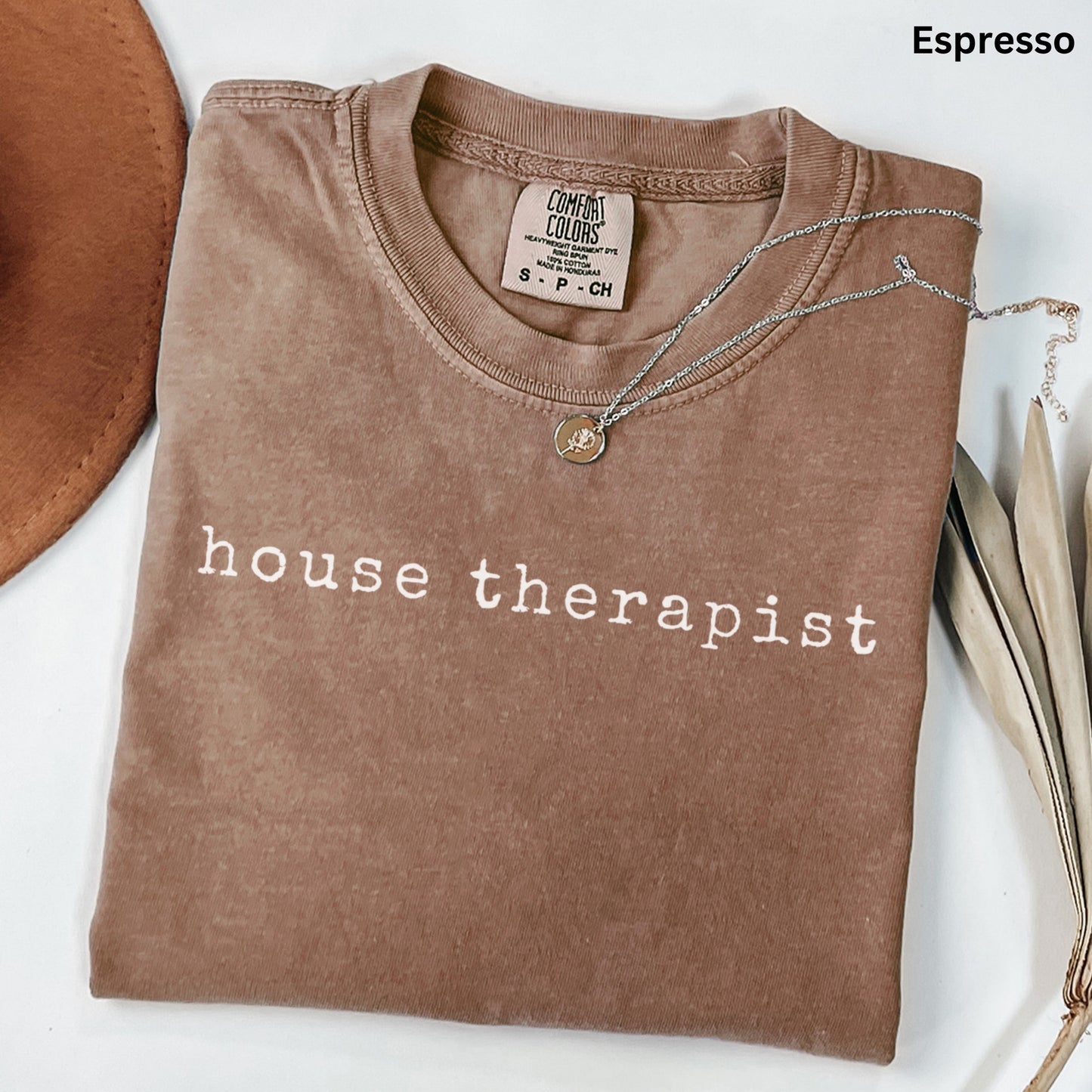 a brown t-shirt with the text "house therapist" printed on it, along with a necklace and some leaves.