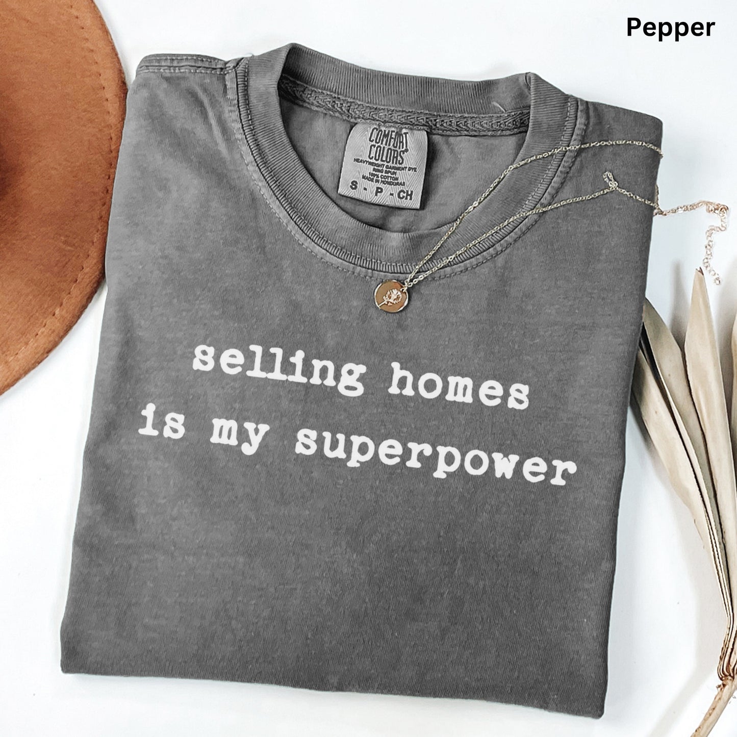 A gray t-shirt with the text "selling homes is my superpower" printed on it, along with a small coin charm.
