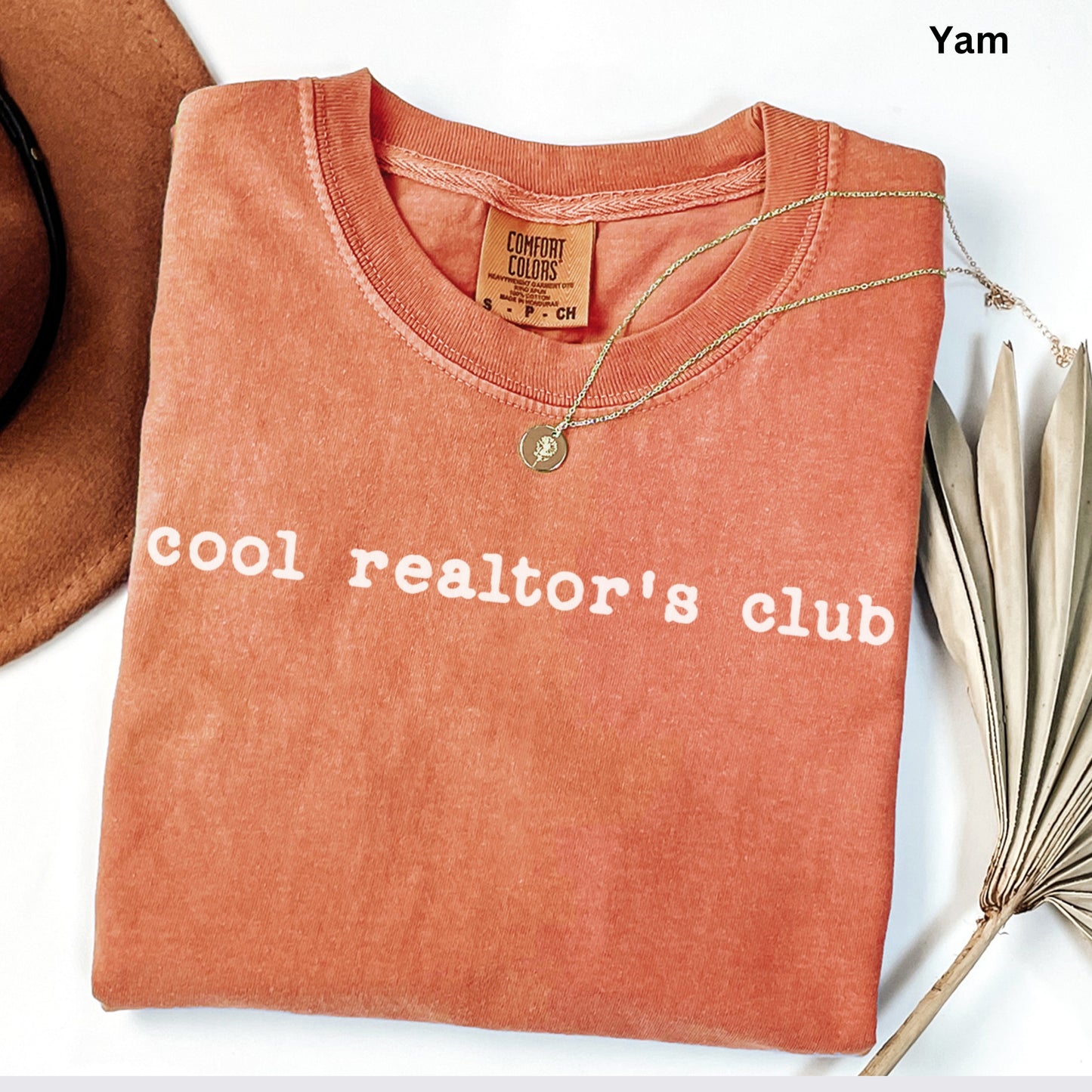 A red t-shirt with the text "cool realtor's club" printed on it, along with a gold necklace and a brown hat.