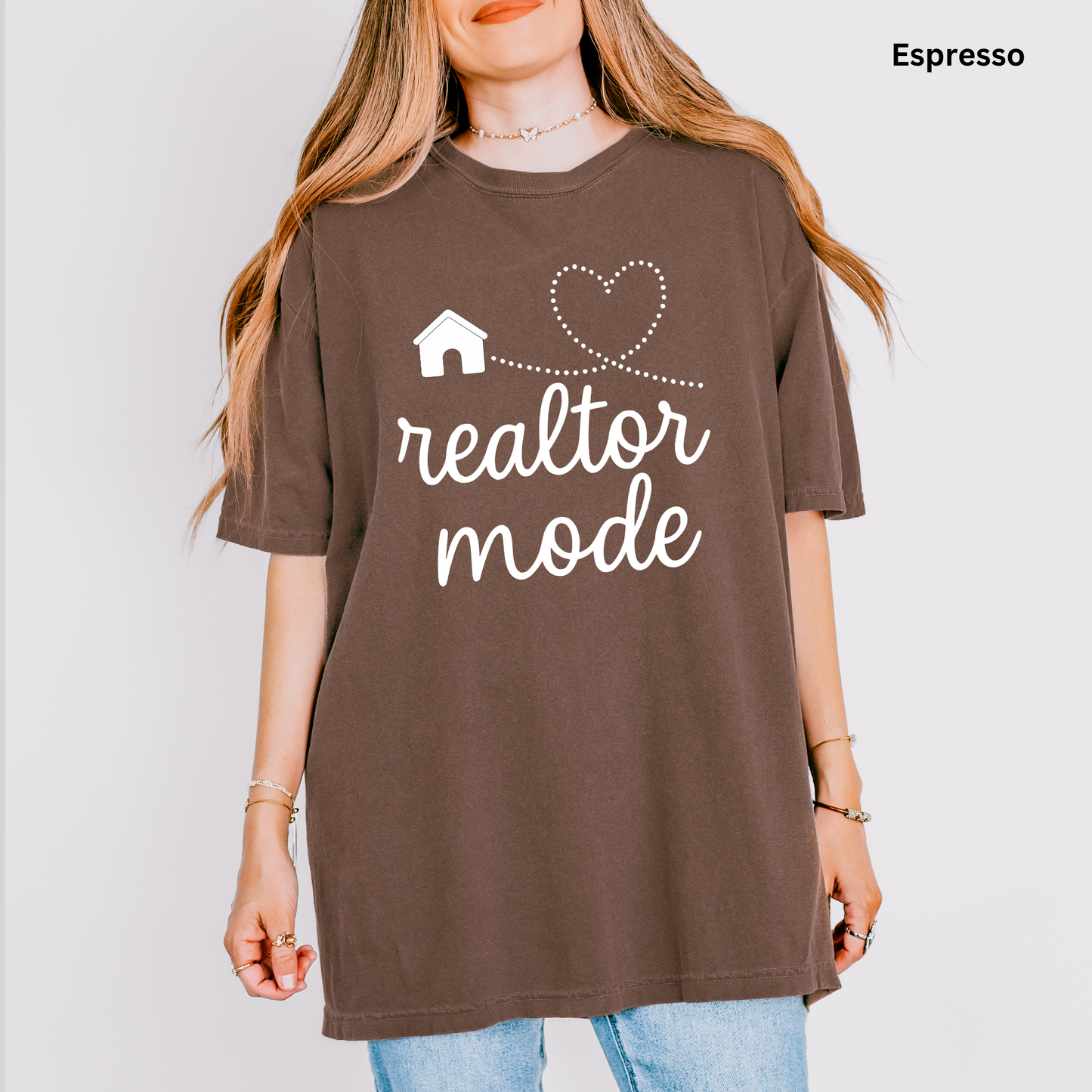 A woman wearing a brown t-shirt with the text "realtor mode" printed on it, along with a heart and house symbol.