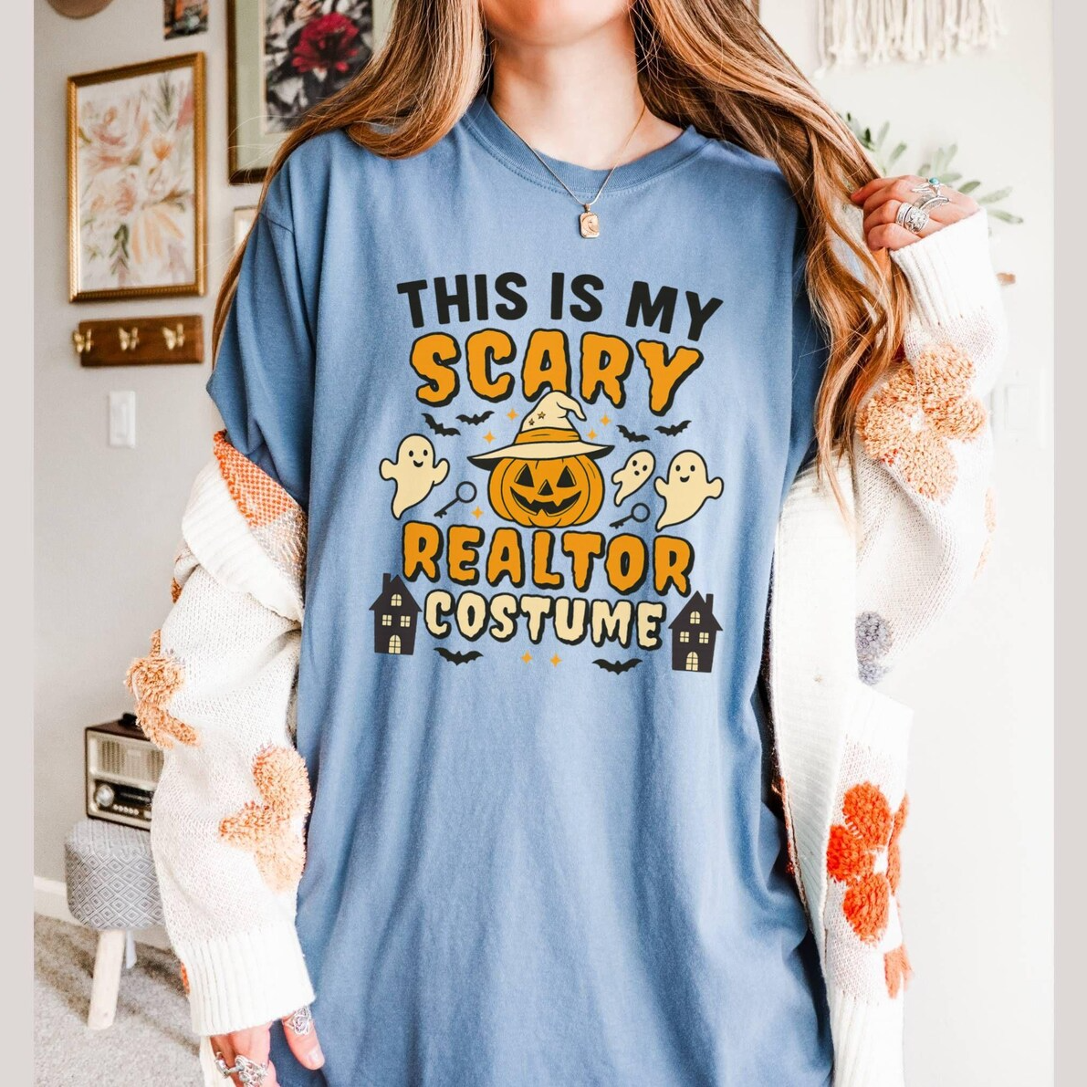 A woman wearing a blue t-shirt with a Halloween-themed design, including a jack-o-lantern, ghost, and a house.
