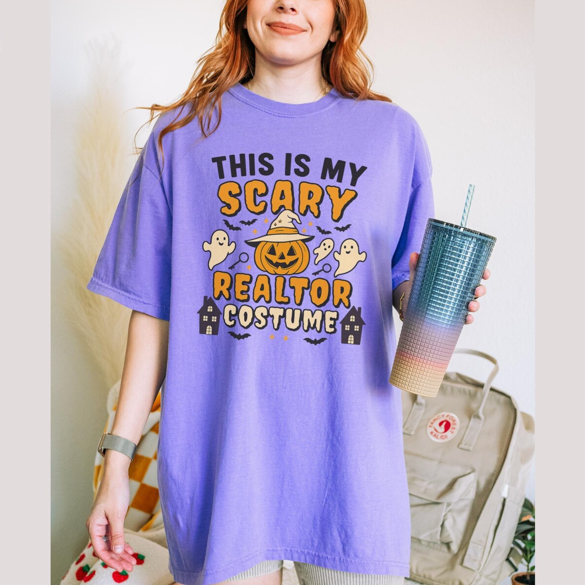 A woman wearing a purple t-shirt with a Halloween-themed design and holding a drink.