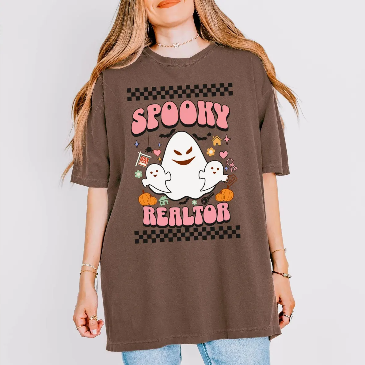A woman wearing a brown t-shirt with a graphic design featuring a ghost character and the text "SPOKEY REALTOR".