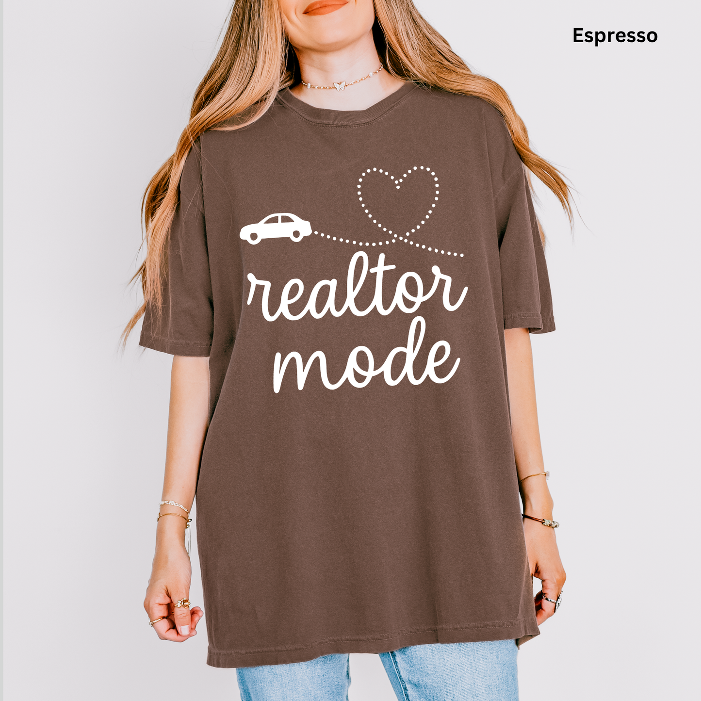 A woman wearing a brown t-shirt with the text "realtor mode" printed on it, along with a heart symbol and a car icon.
