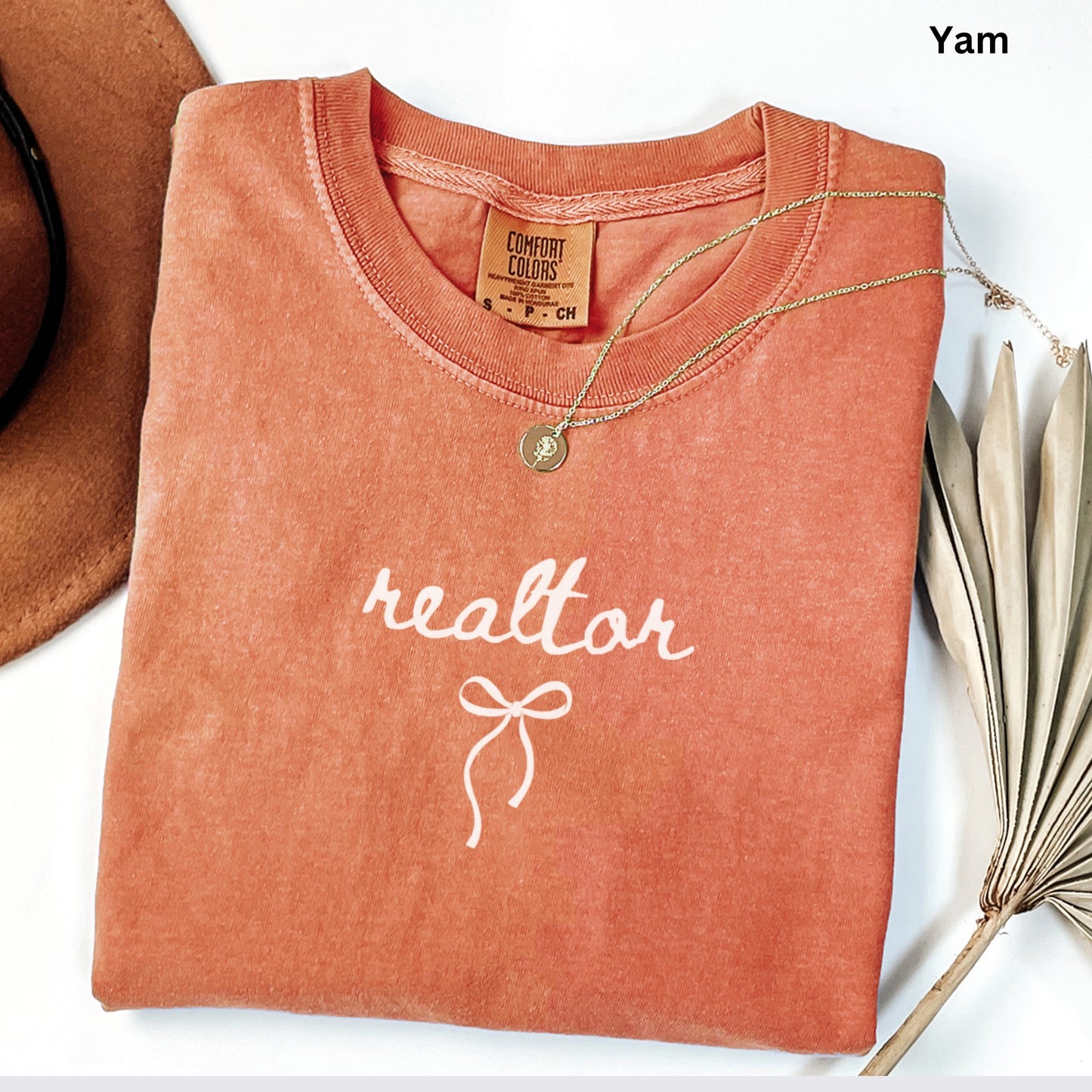 a red t-shirt with the word "realtor" printed on it, along with a gold necklace and a brown hat.