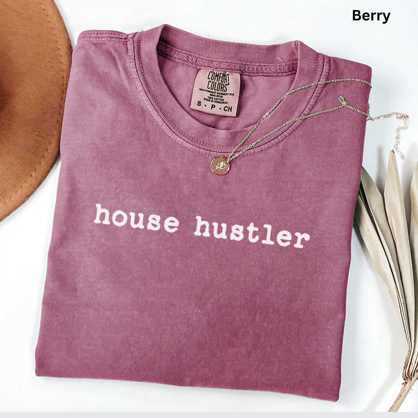 A pink t-shirt with the text "house hustler" printed on it, along with a necklace and a hat.