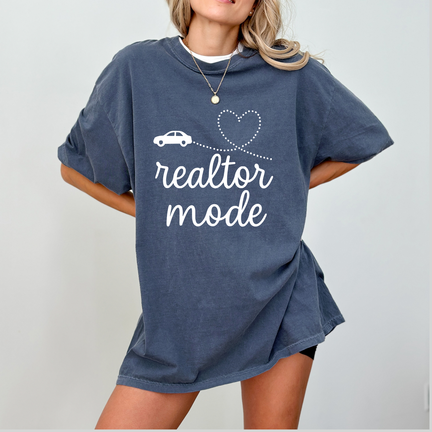 A woman wearing a blue t-shirt with the text "realtor mode" printed on it, standing against a white background.