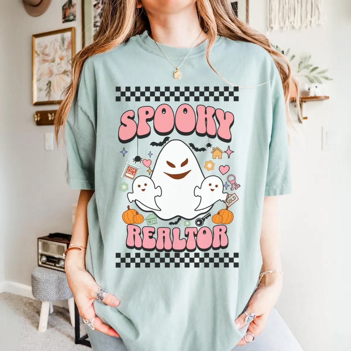 A woman wearing a light blue t-shirt with a graphic design featuring a ghost character and the text "SPOKEY REALTOR".