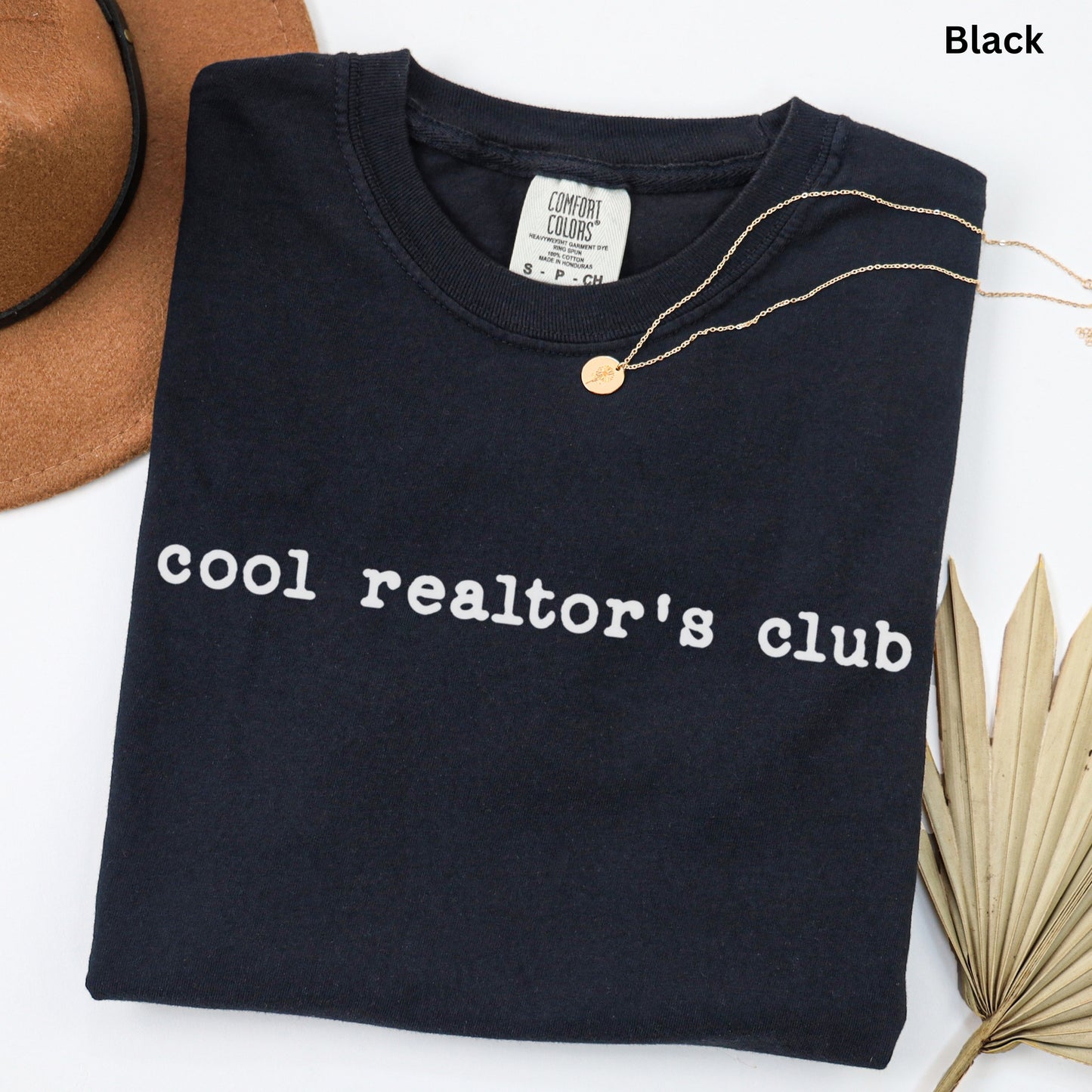 A black t-shirt with the text "cool realtor's club" printed on it, along with a gold necklace and a brown hat.