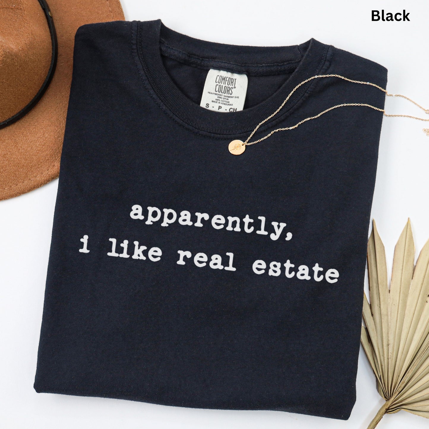a black t-shirt with white text that reads "apparently, I like real estate" and a gold necklace.