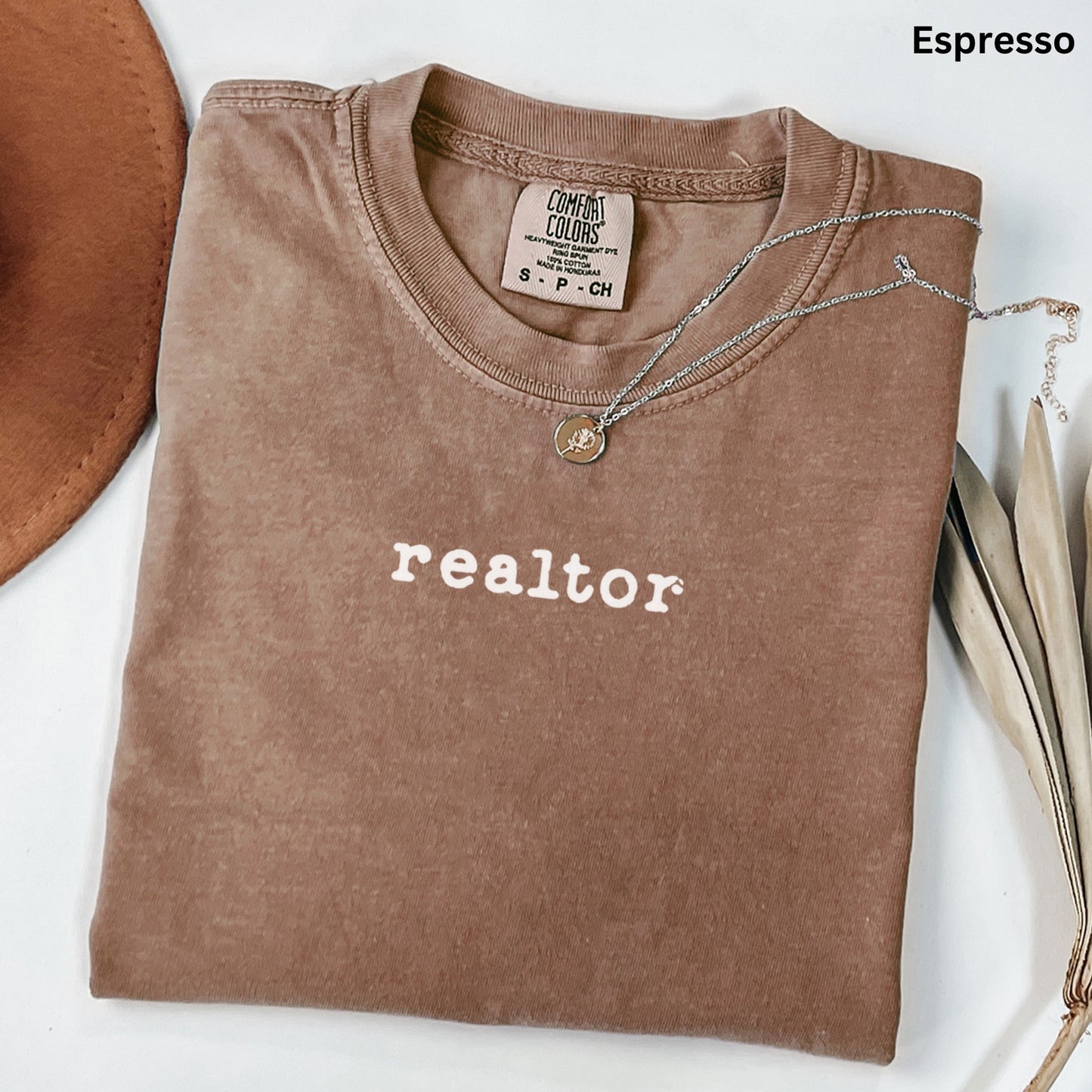 a brown t-shirt with the word "realtor" printed on it, along with a necklace and some leaves.