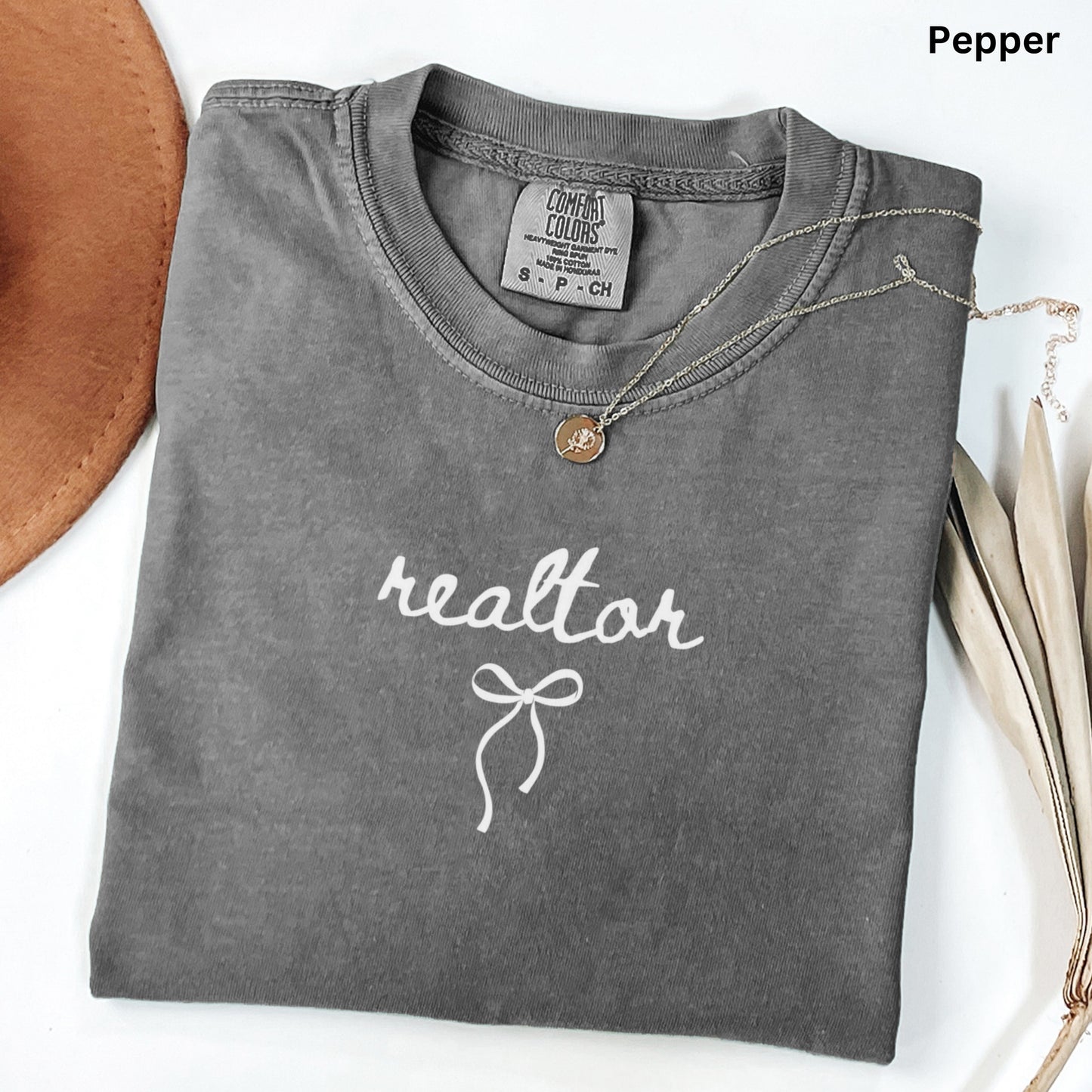 A gray t-shirt with the word "realtor" printed on it, along with a small charm necklace and a brown hat.