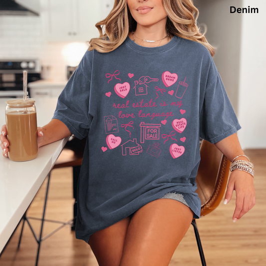 A woman wearing a blue t-shirt with a graphic design printed on it, sitting at a table with a drink in a glass.