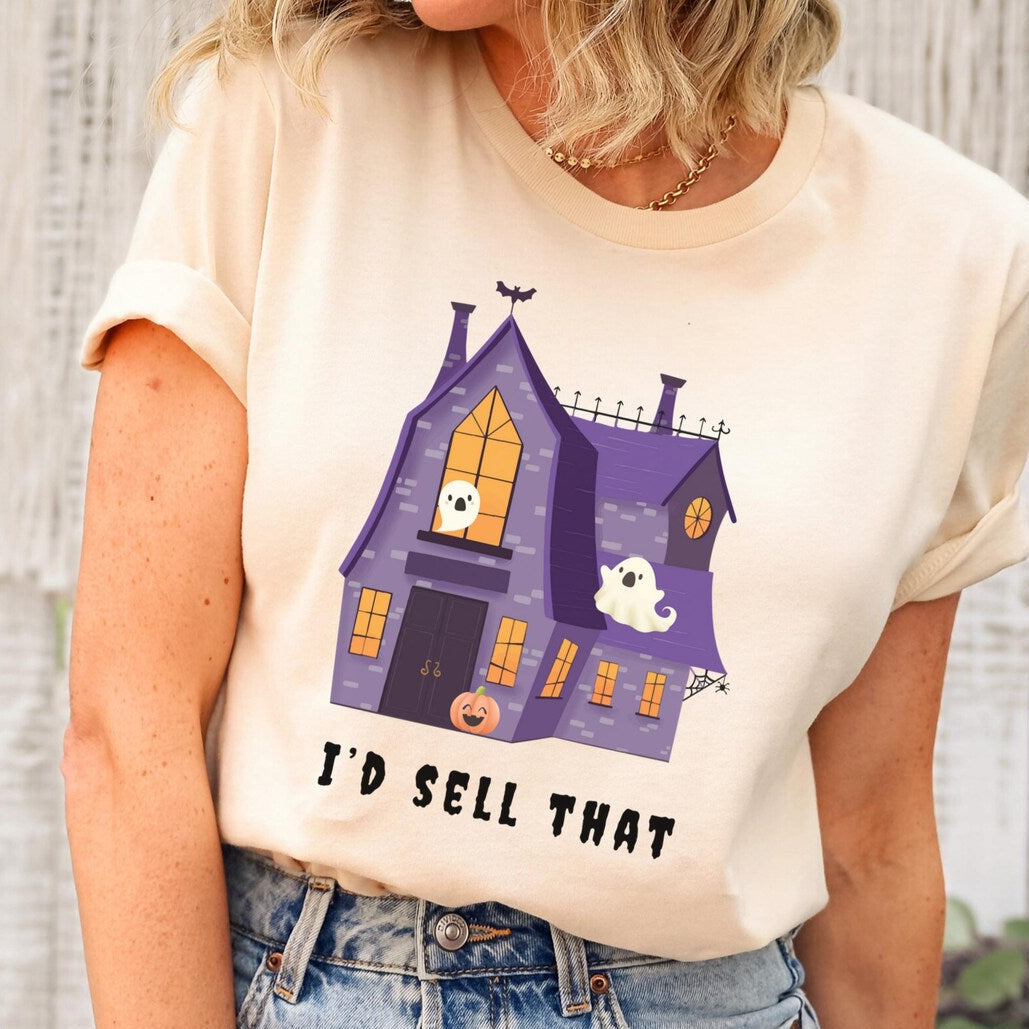 Person wearing a t-shirt with a haunted house graphic and text, standing against a wooden wall.