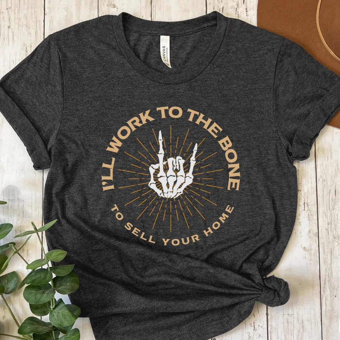 Dark gray heather t-shirt with graphic design and text on a wooden surface with plants.