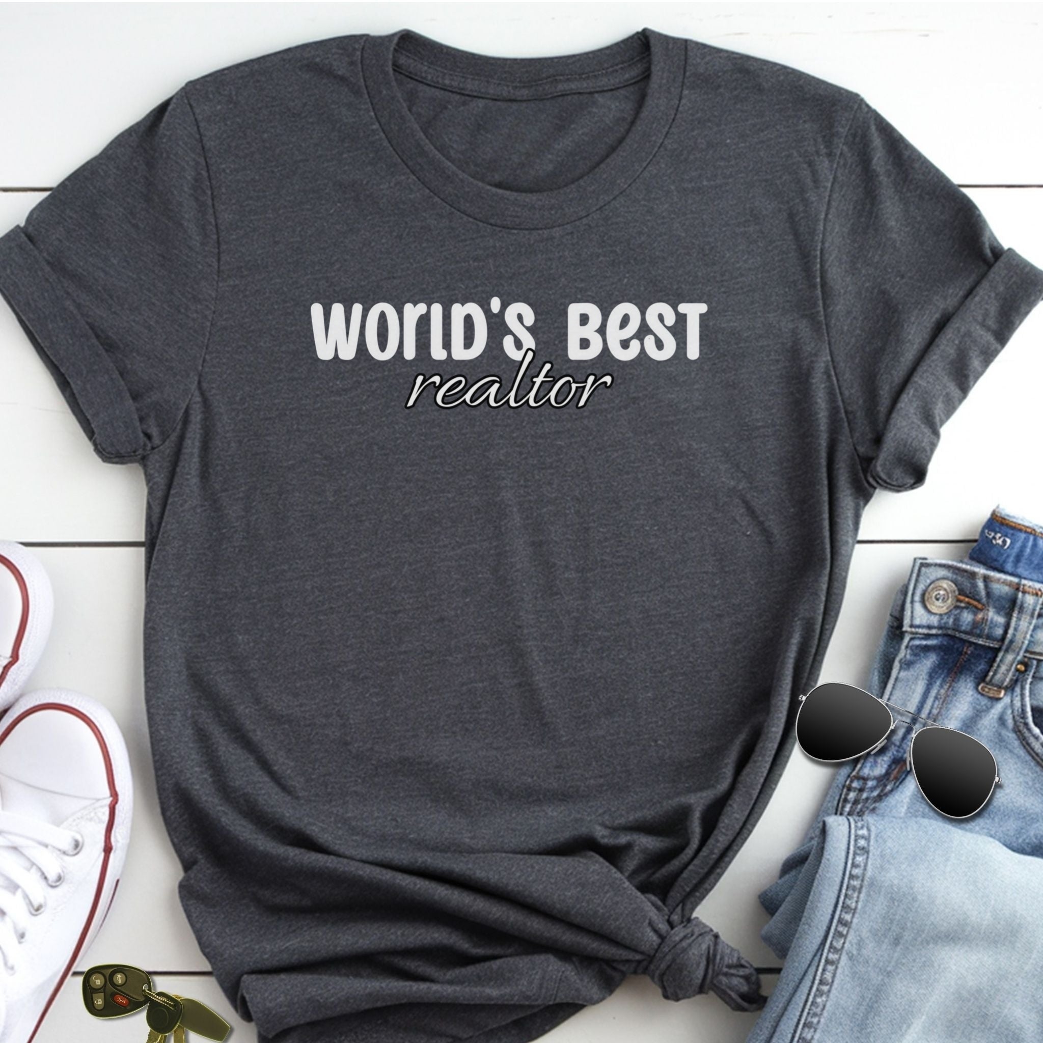 A gray t-shirt with the text "WORLD'S BEST REALTOR" printed on it, along with a pair of jeans and sunglasses.