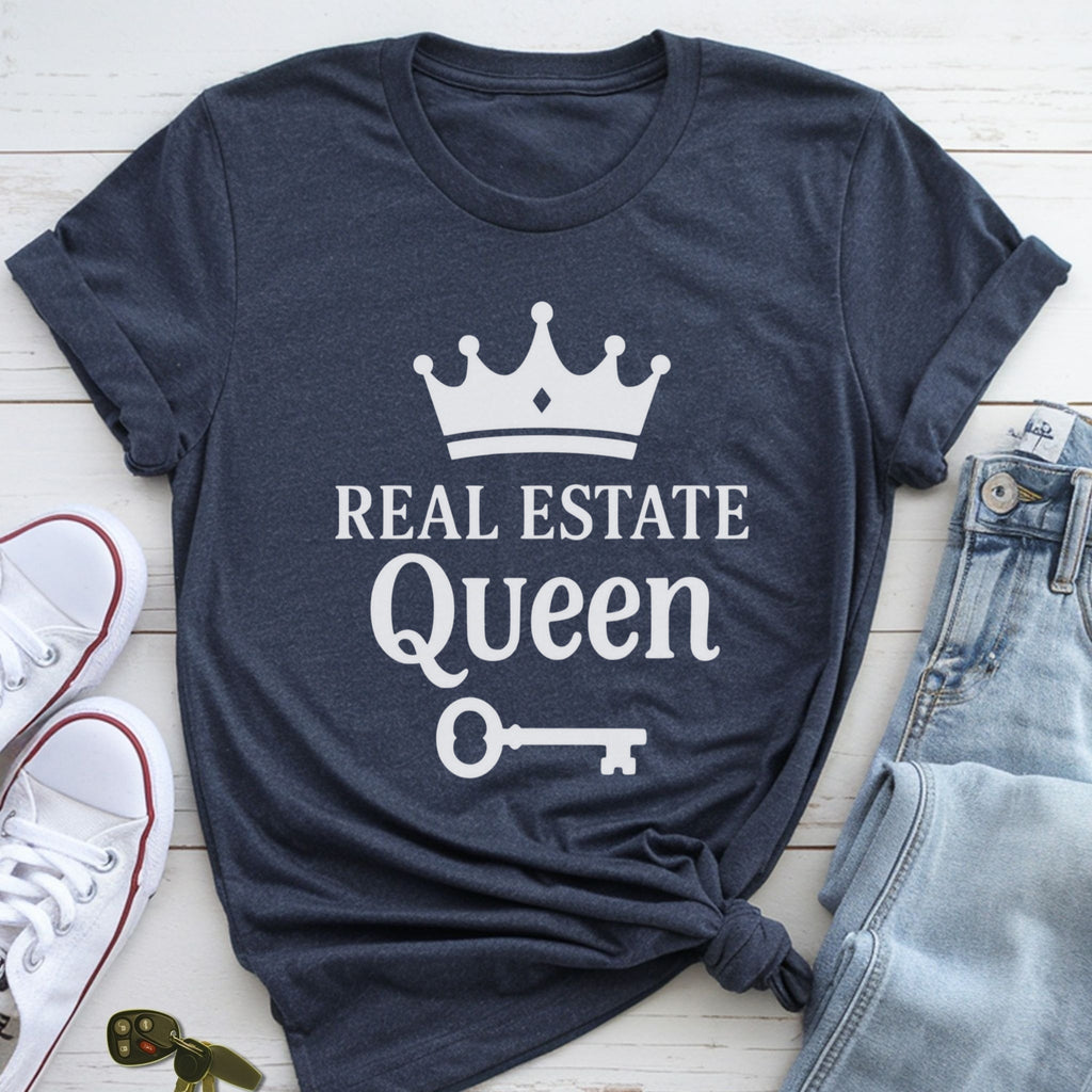 A navy blue t-shirt with the text "REAL ESTATE QUEEN" printed on it, along with a crown and a key, is displayed on a wooden surface alongside a pair of jeans and white sneakers.