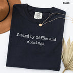 A black t-shirt with the text "fueled by coffee and closings" printed on it, along with a gold necklace and a brown hat.
