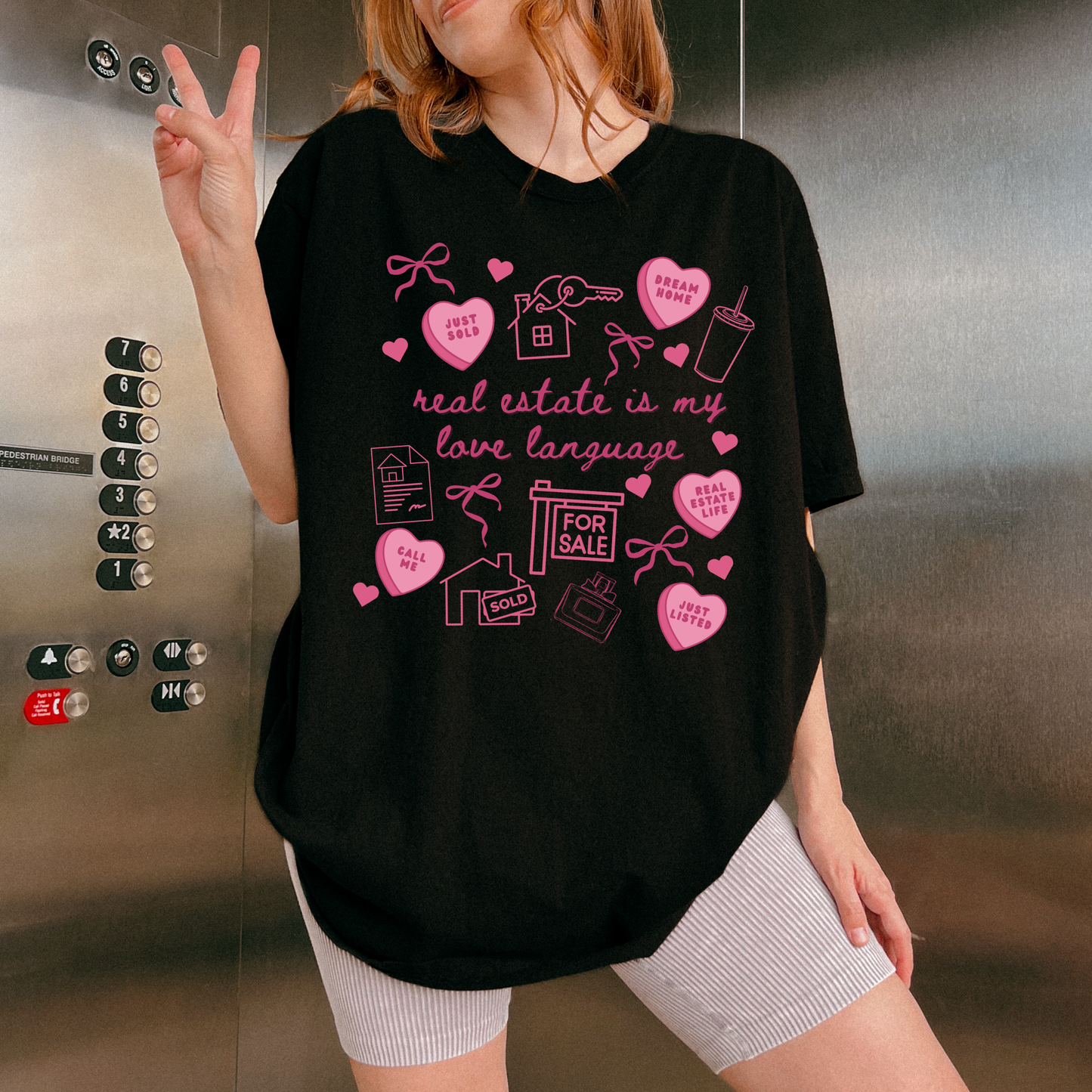 A woman wearing a black t-shirt with a message about real estate, and she is making a peace sign with her hand.
