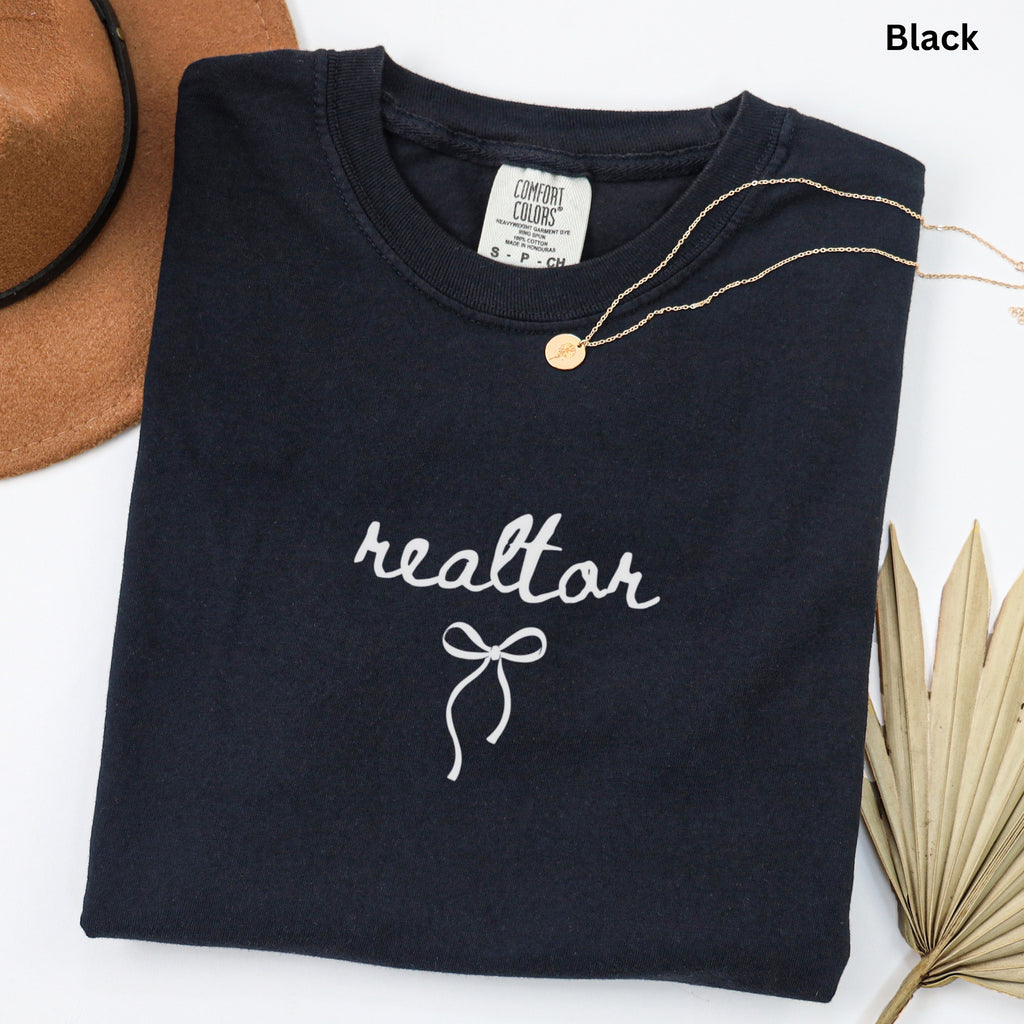 a black t-shirt with the word "realtor" printed on it, along with a gold necklace and a brown hat.