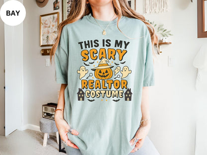 A person wearing a light blue t-shirt with a Halloween-themed design, including a jack-o-lantern, ghost, and houses.