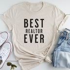 A beige t-shirt with the text "BEST REALTOR EVER" printed on it, along with a pair of jeans and white sneakers.