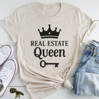 a beige t-shirt with the text "REAL ESTATE QUEEN" printed on it, along with a crown and a key symbol. The t-shirt is laid out on a white surface, accompanied by a pair of jeans, a pair of sneakers, and a set of keys.