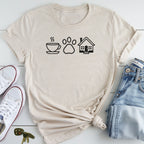 A beige t-shirt with a graphic design of a coffee cup, a paw print, and a house, along with a pair of jeans and sneakers, all laid out on a white surface.
