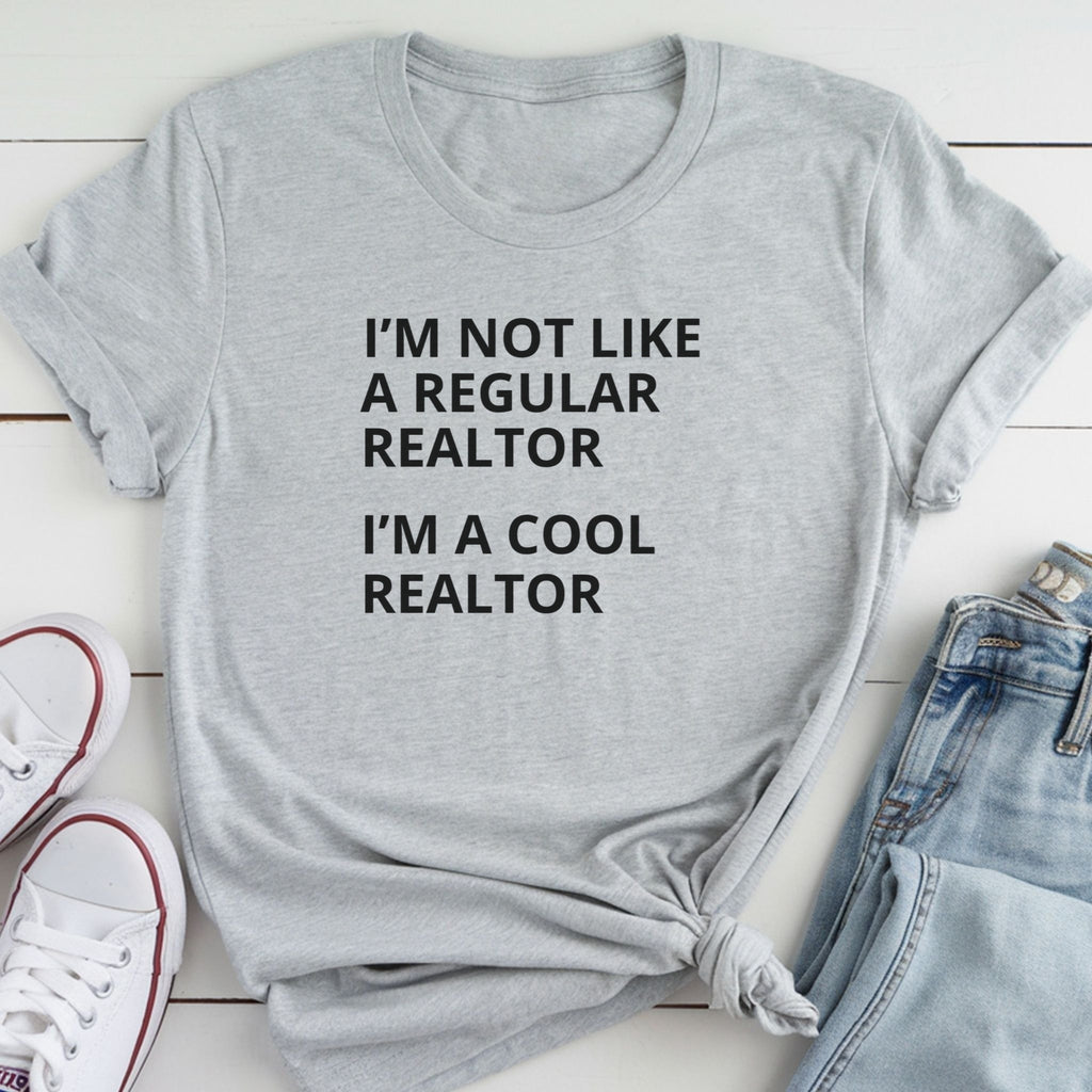 A gray t-shirt with the text "I'M NOT LIKE A REGULAR REALTOR I'M A COOL REALTOR" printed on it, along with a pair of jeans and white sneakers.