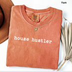 a red t-shirt with the text "house hustler" printed on it, along with a necklace and a hat.