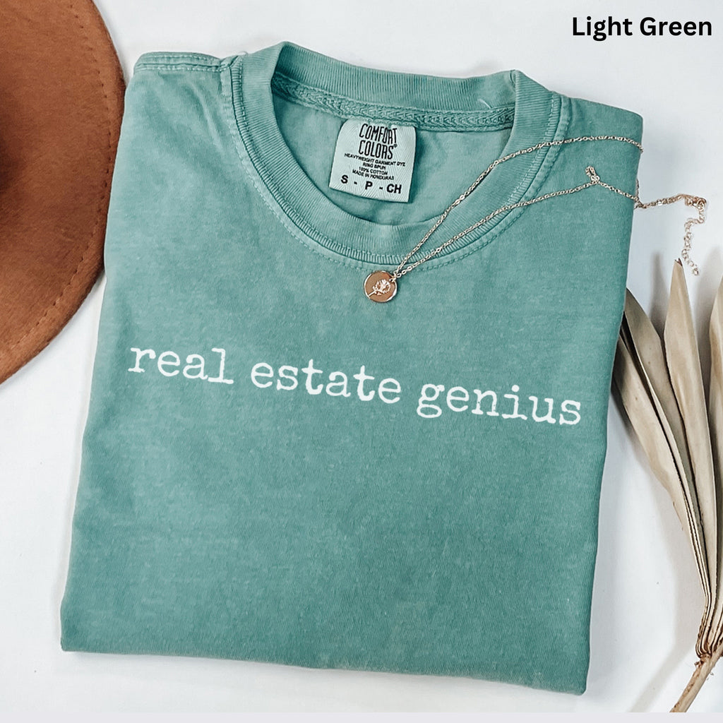 A light green t-shirt with the text "real estate genius" printed on it, along with a necklace and a brown hat.