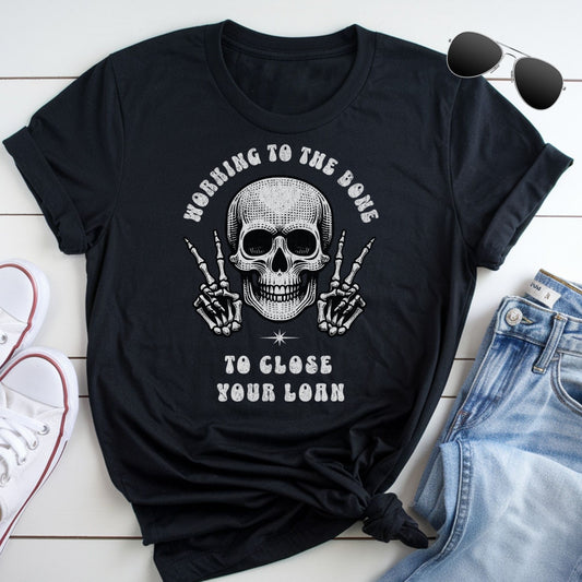 A black t-shirt with a skull graphic and the text "Working to the bone to close your home" printed on it, along with a pair of jeans and sunglasses.