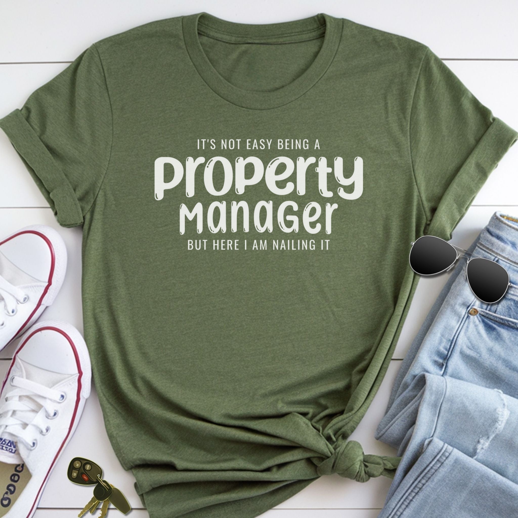 A green t-shirt with a humorous text printed on it, along with a pair of sunglasses, a pair of jeans, and a pair of white sneakers.