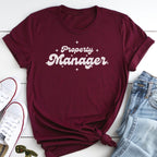 A burgundy t-shirt with the text "Property Manager" printed on it, along with a pair of jeans and white sneakers.