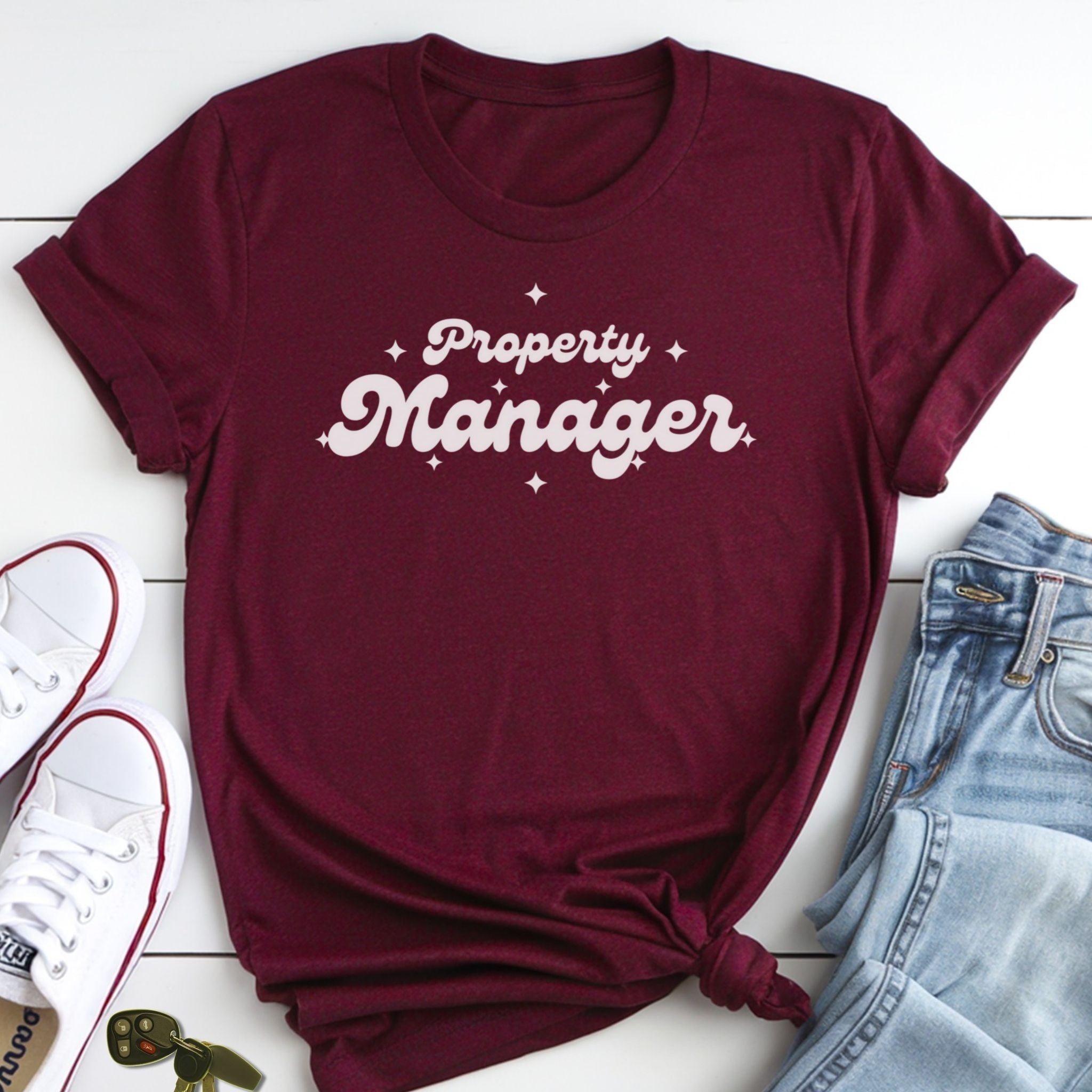 A burgundy t-shirt with the text "Property Manager" printed on it, along with a pair of jeans and white sneakers.