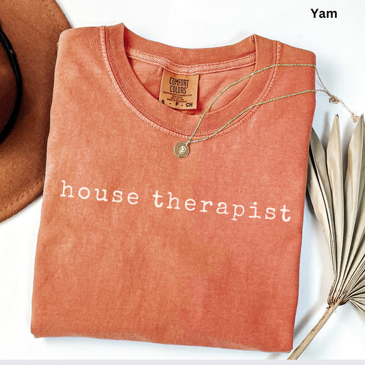 a red t-shirt with the text "house therapist" printed on it, along with a necklace and a hat.