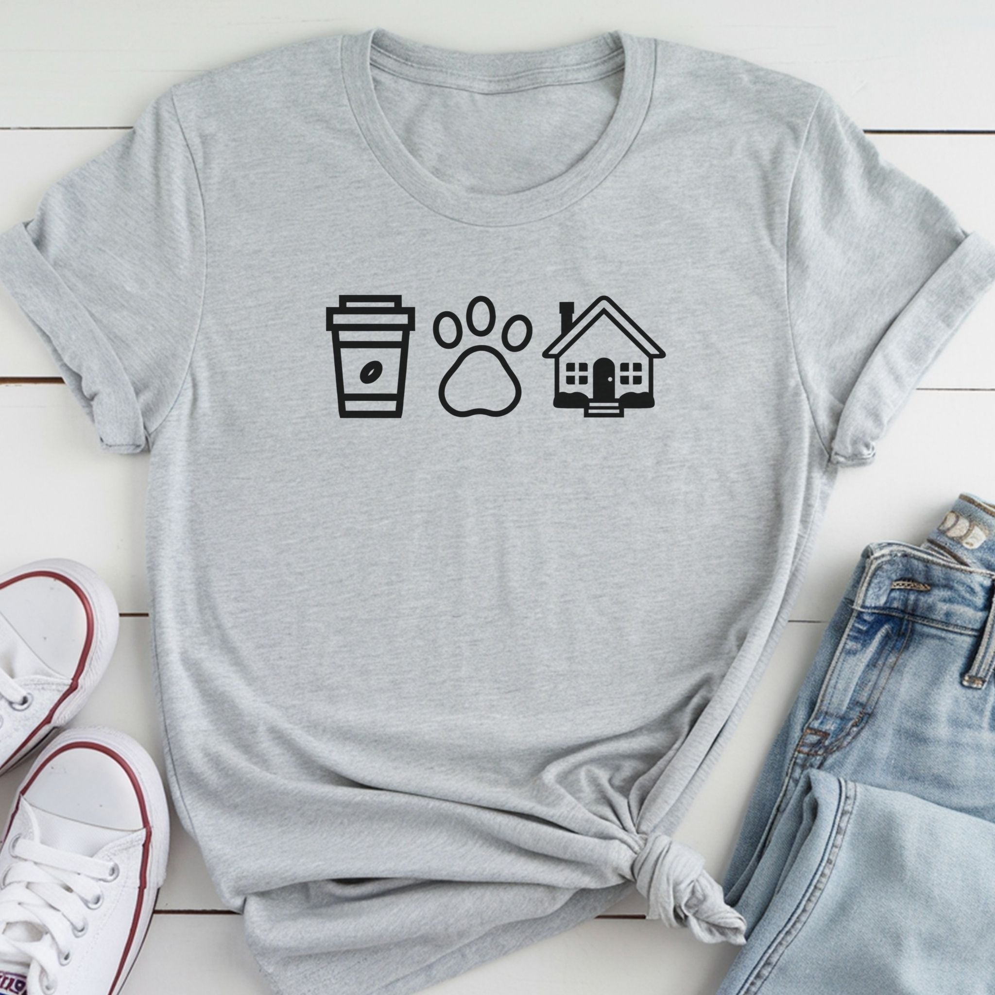 A gray t-shirt with a graphic design of a coffee cup, paw print, and house, along with a pair of jeans and white sneakers.