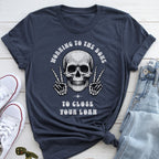 A dark blue t-shirt with a skull graphic and text, along with a pair of jeans and sneakers, laid out on a white surface.