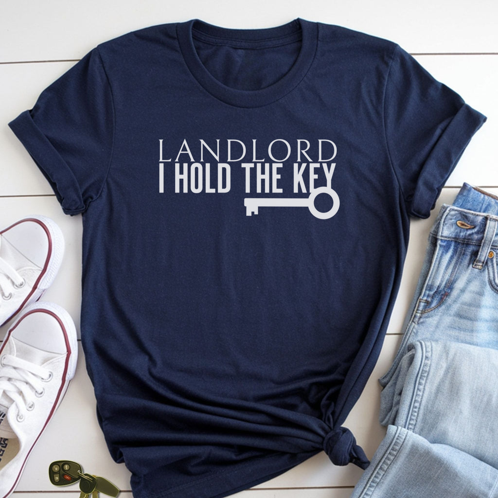 A navy blue t-shirt with the text "LANDLORD I HOLD THE KEY" printed on it, along with a key graphic. The t-shirt is placed on a white surface, and there are a pair of jeans and a pair of white sneakers visible in the image.