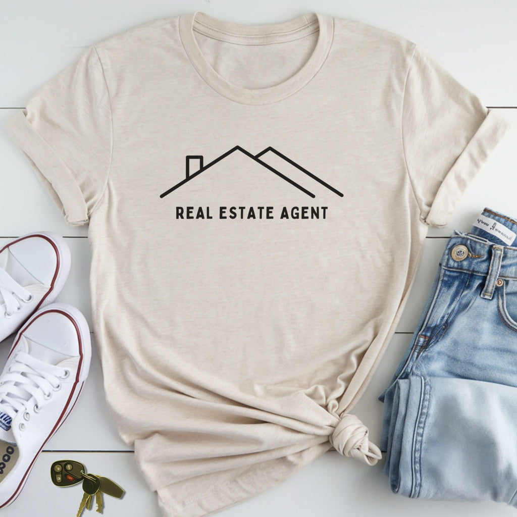 a beige t-shirt with a graphic design of a house and the text "REAL ESTATE AGENT" printed on it, along with a pair of jeans and sneakers.